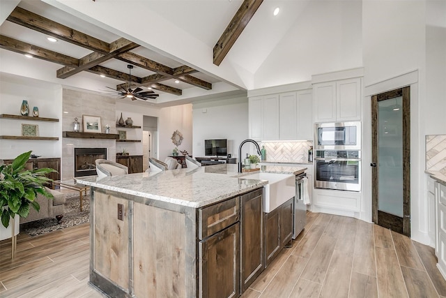 kitchen featuring light stone counters, backsplash, appliances with stainless steel finishes, a fireplace, and wood tiled floor