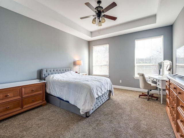 carpeted bedroom with a tray ceiling, multiple windows, and baseboards