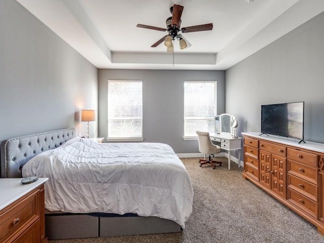 bedroom with a tray ceiling, light carpet, baseboards, and ceiling fan