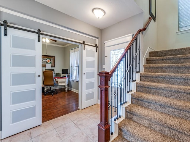 stairs with tile patterned flooring, a barn door, crown molding, and baseboards