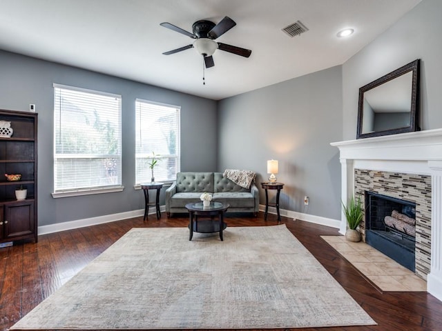 living area with visible vents, ceiling fan, baseboards, a tiled fireplace, and wood finished floors