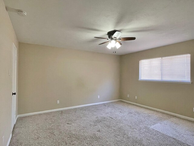 carpeted spare room with a ceiling fan and baseboards