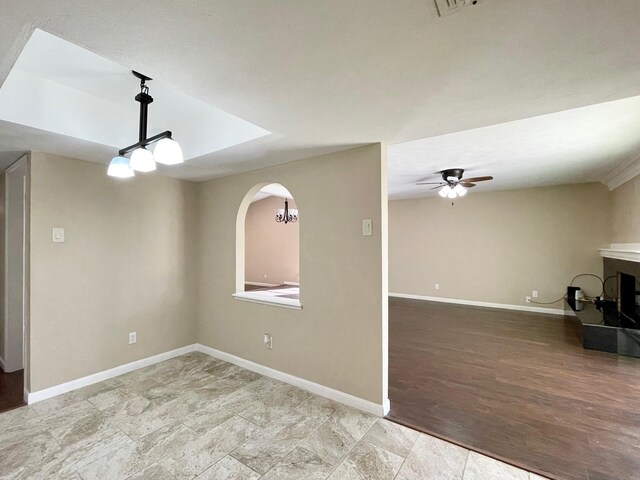 empty room featuring arched walkways, ceiling fan with notable chandelier, baseboards, and wood finished floors