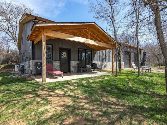 back of property with a patio, a garage, a lawn, and stone siding