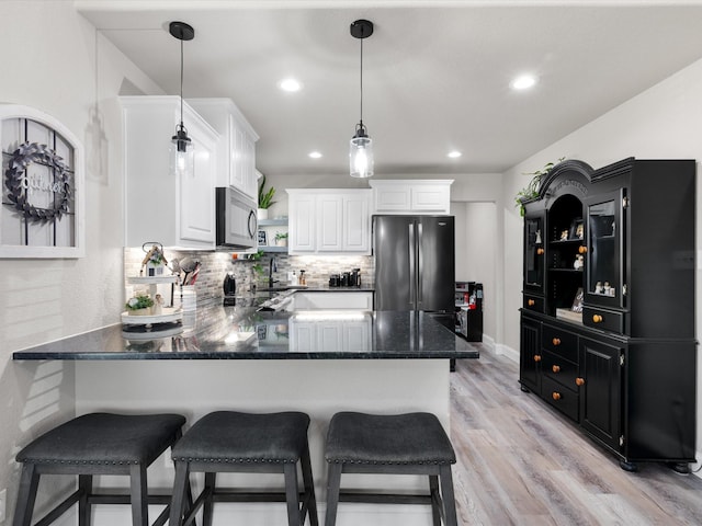 kitchen featuring a peninsula, freestanding refrigerator, stainless steel microwave, light wood-type flooring, and backsplash