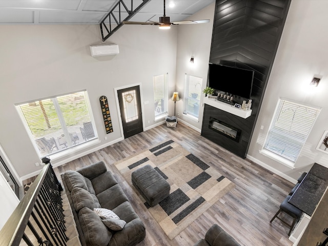 living area with wood finished floors, a ceiling fan, baseboards, high vaulted ceiling, and a large fireplace