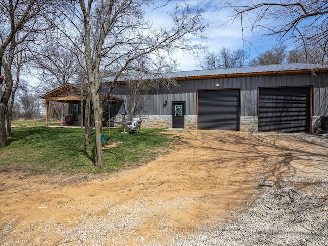 view of front of home featuring board and batten siding, a detached garage, metal roof, an outdoor structure, and driveway