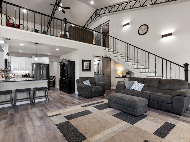 living room featuring stairway, dark wood-style floors, baseboards, a towering ceiling, and a barn door