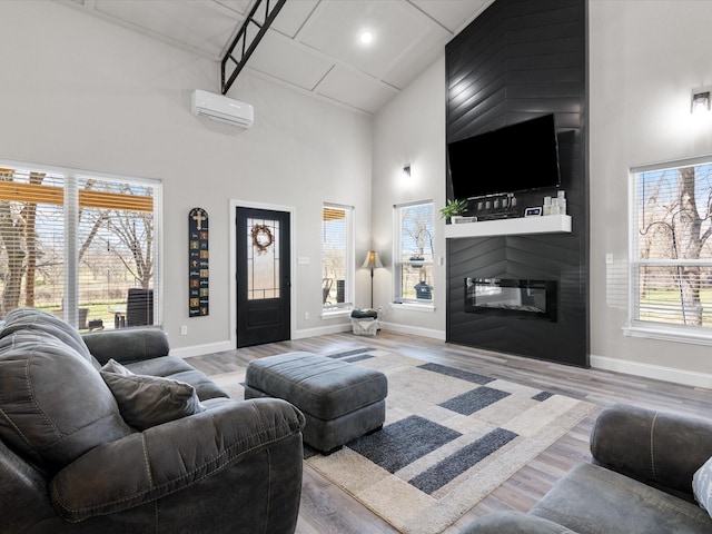 living room featuring a large fireplace, a wall mounted air conditioner, a high ceiling, and wood finished floors