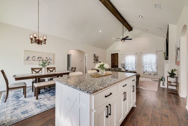 kitchen featuring light stone countertops, dark wood finished floors, beam ceiling, arched walkways, and a center island