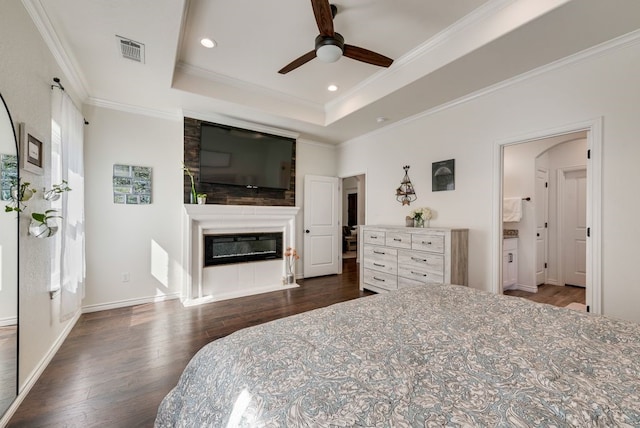 bedroom featuring visible vents, ornamental molding, wood finished floors, a glass covered fireplace, and a raised ceiling