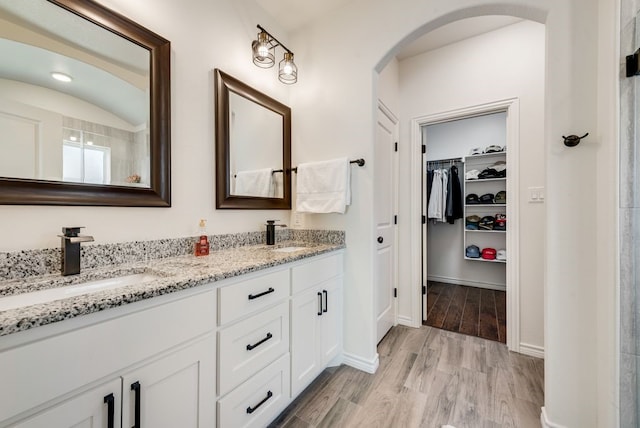 full bathroom featuring double vanity, wood finished floors, a walk in closet, and a sink