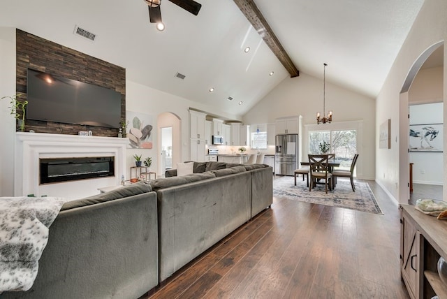 living room with visible vents, high vaulted ceiling, dark wood-style flooring, a glass covered fireplace, and beamed ceiling