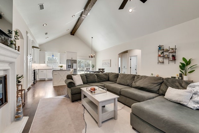 living area featuring light wood finished floors, high vaulted ceiling, beam ceiling, arched walkways, and a glass covered fireplace