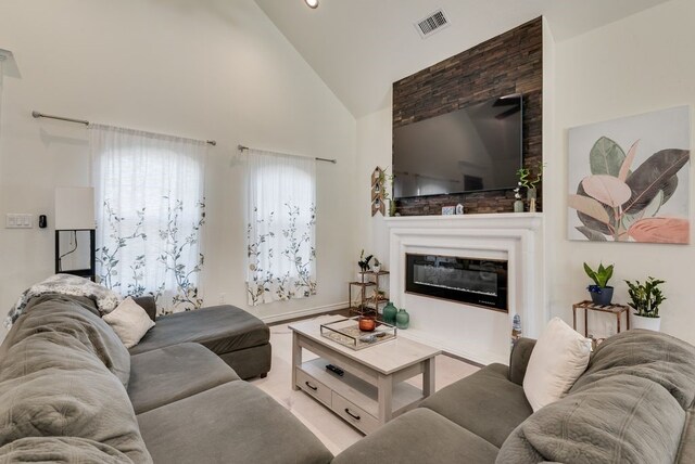 living area featuring a glass covered fireplace, visible vents, and high vaulted ceiling