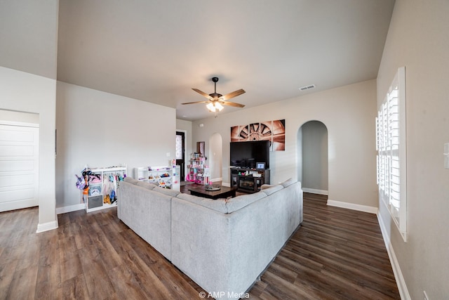 living room featuring arched walkways, plenty of natural light, dark wood-style floors, and a ceiling fan