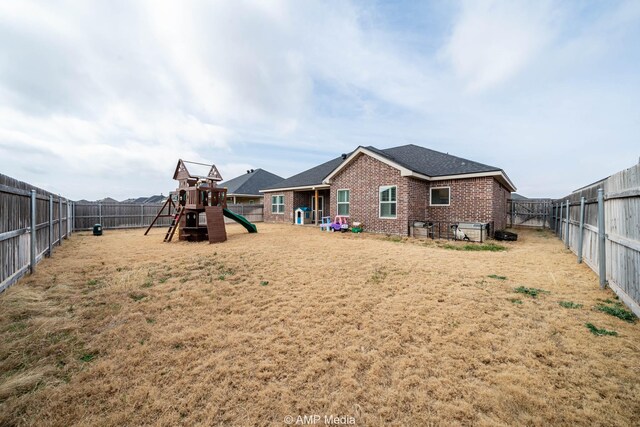 back of property with brick siding, a lawn, a playground, and a fenced backyard