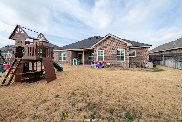 back of house with brick siding, a playground, fence, roof with shingles, and a yard