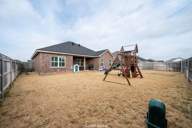 back of property featuring central AC unit, a playground, a fenced backyard, and brick siding