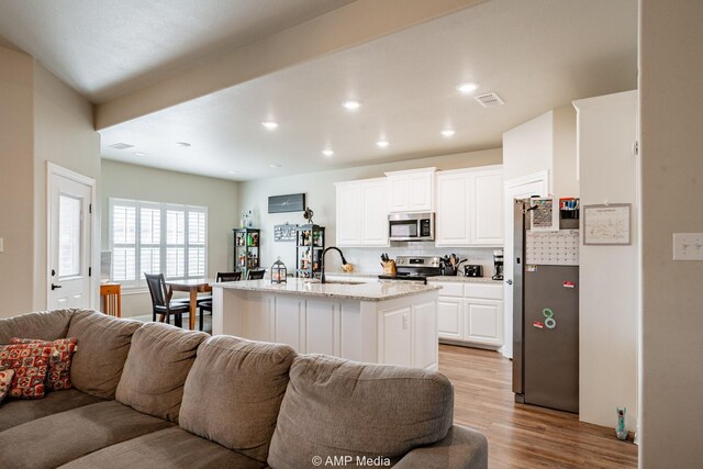 kitchen featuring a sink, stainless steel appliances, open floor plan, light wood-style floors, and tasteful backsplash