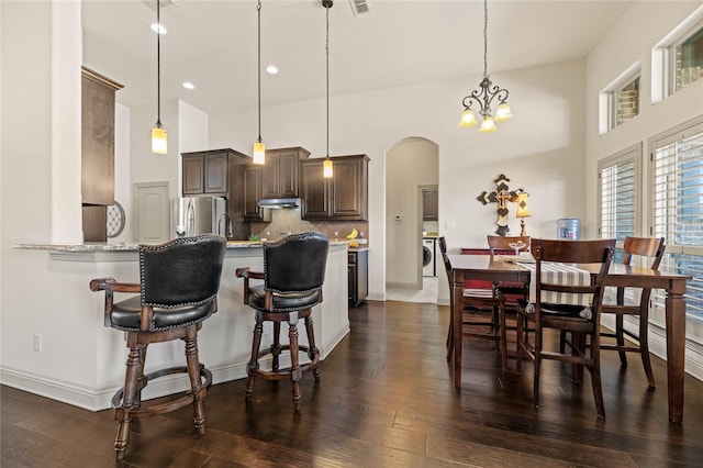 kitchen with arched walkways, freestanding refrigerator, dark wood-style flooring, decorative backsplash, and independent washer and dryer