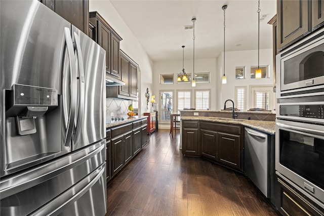 kitchen with a sink, dark brown cabinetry, decorative backsplash, stainless steel appliances, and dark wood-style flooring