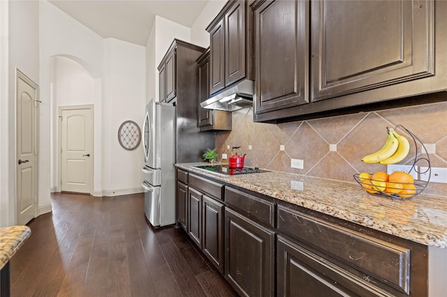 kitchen featuring arched walkways, freestanding refrigerator, dark wood-type flooring, under cabinet range hood, and black electric stovetop