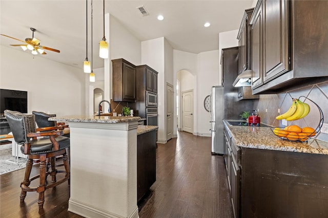 kitchen with light stone counters, dark wood-style floors, arched walkways, stainless steel appliances, and dark brown cabinets