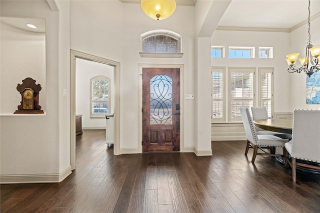 foyer entrance featuring baseboards, dark wood finished floors, arched walkways, ornamental molding, and a chandelier