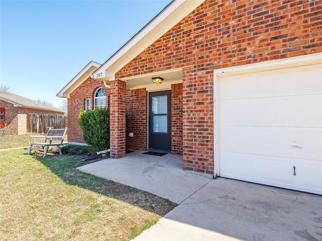 view of exterior entry with brick siding, an attached garage, and fence