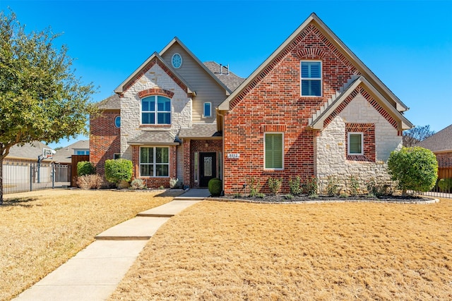 view of front of house featuring brick siding, stone siding, a front yard, and fence