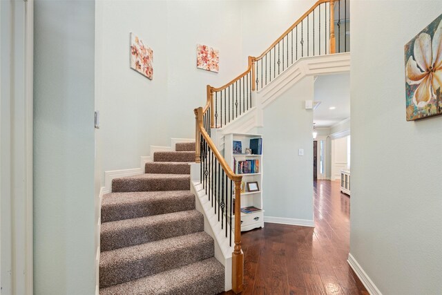 staircase with hardwood / wood-style floors, a high ceiling, and baseboards