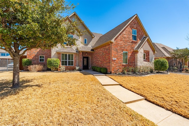 traditional home featuring a front yard, fence, brick siding, and roof with shingles