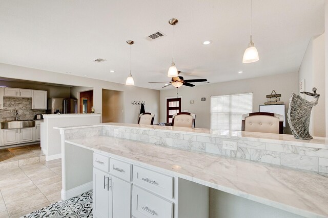 kitchen featuring decorative backsplash, visible vents, stainless steel refrigerator with ice dispenser, and a sink