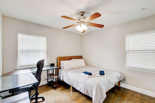 bedroom featuring multiple windows, a ceiling fan, baseboards, and wood finished floors