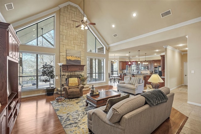 living area featuring a stone fireplace, high vaulted ceiling, visible vents, and ornamental molding