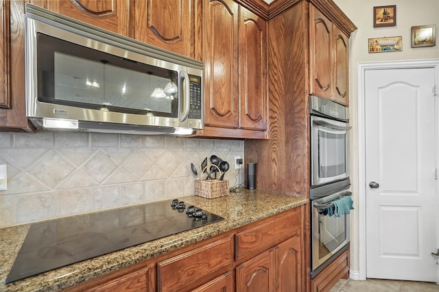 kitchen featuring tasteful backsplash, light stone countertops, light tile patterned floors, brown cabinets, and stainless steel appliances