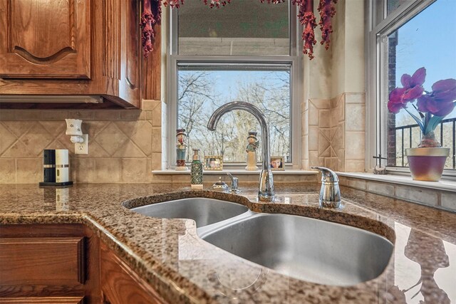 interior details featuring brown cabinetry, stone countertops, backsplash, and a sink