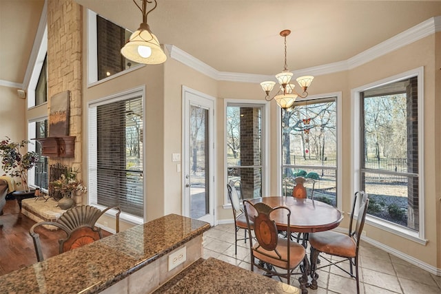 dining space with baseboards, ornamental molding, a stone fireplace, an inviting chandelier, and light tile patterned flooring