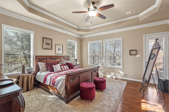 bedroom with visible vents, ornamental molding, a raised ceiling, and wood finished floors