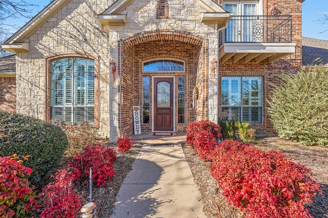 doorway to property with stone siding, brick siding, and a balcony