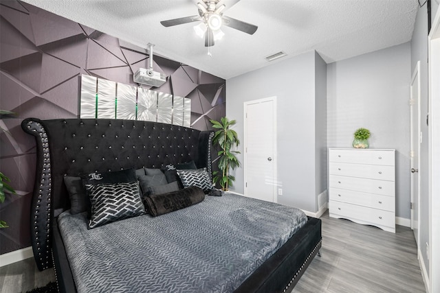 bedroom with visible vents, a textured ceiling, baseboards, and wood finished floors