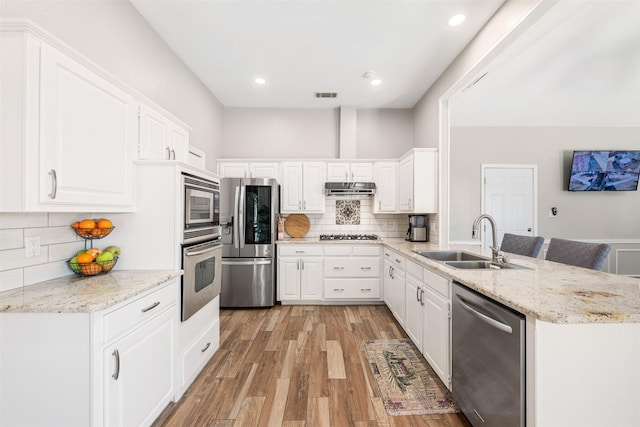 kitchen with visible vents, under cabinet range hood, appliances with stainless steel finishes, a peninsula, and a sink