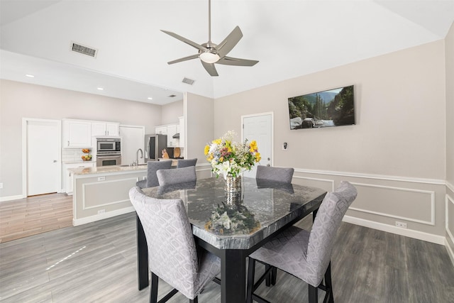 dining space featuring ceiling fan, visible vents, light wood-style flooring, and wainscoting