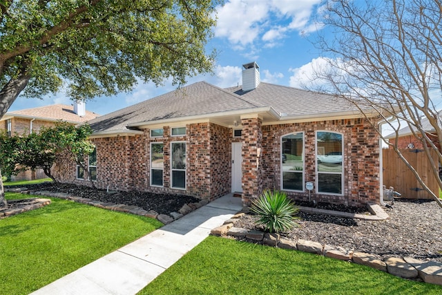 ranch-style home featuring brick siding, a chimney, a front lawn, and roof with shingles