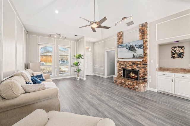 living area with a brick fireplace, wood finished floors, track lighting, and a decorative wall