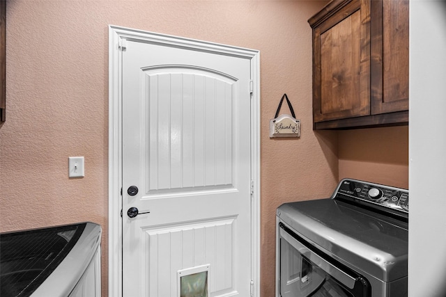 clothes washing area featuring washing machine and clothes dryer, cabinet space, and a textured wall