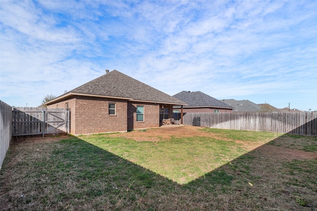 back of property with a lawn, a gate, a fenced backyard, roof with shingles, and brick siding