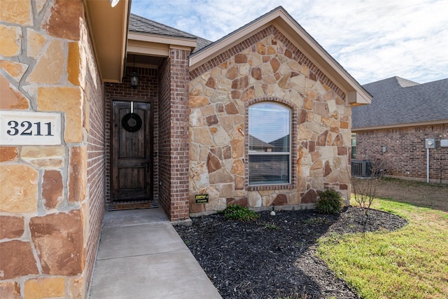 view of exterior entry featuring stone siding, brick siding, and central AC unit