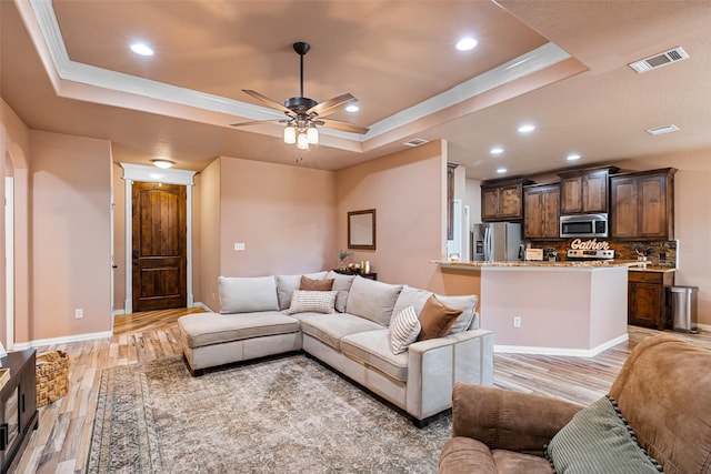 living area with visible vents, a raised ceiling, baseboards, and light wood-style flooring